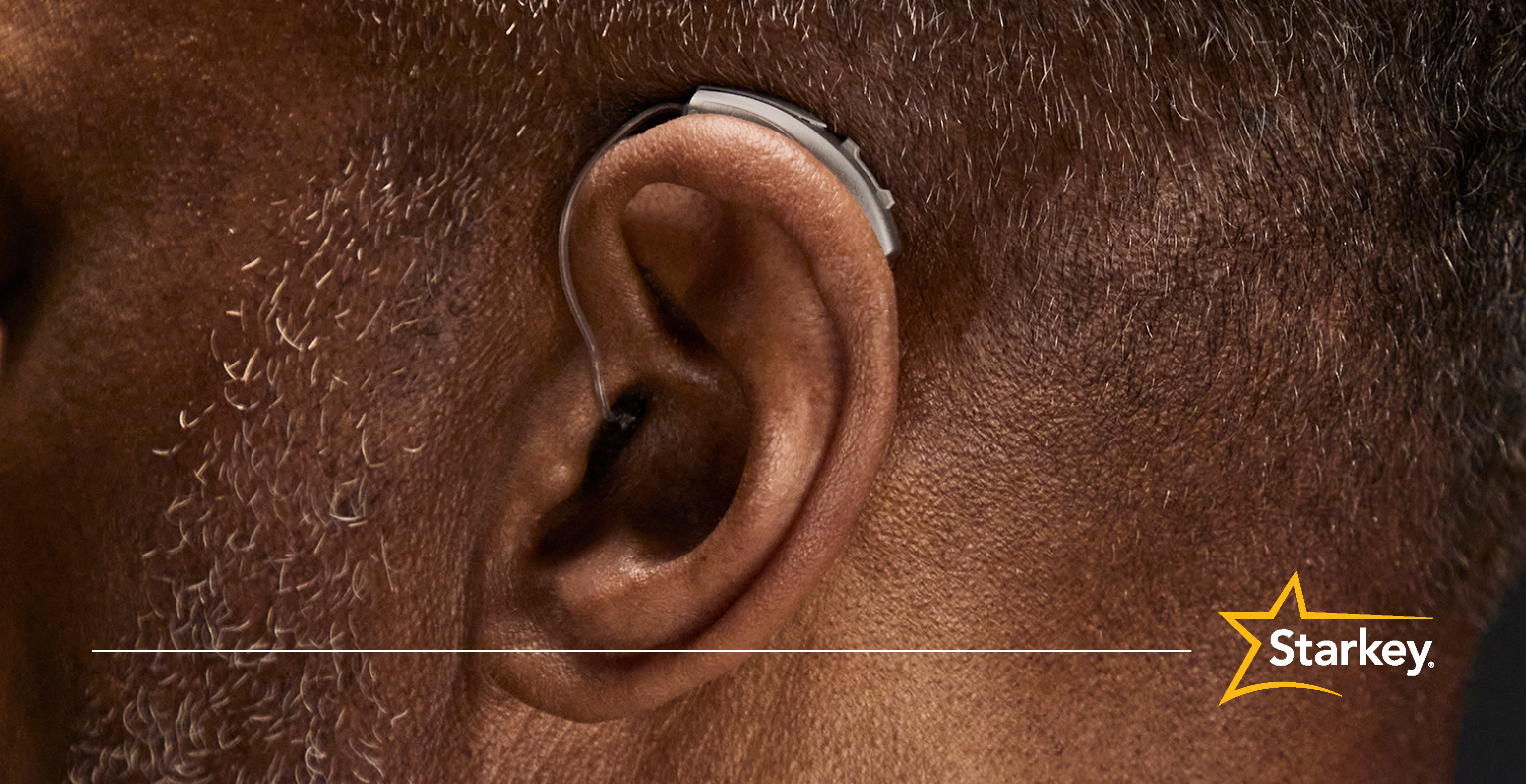 Close up of silver receiver-in-canal hearing aid on a man's left ear